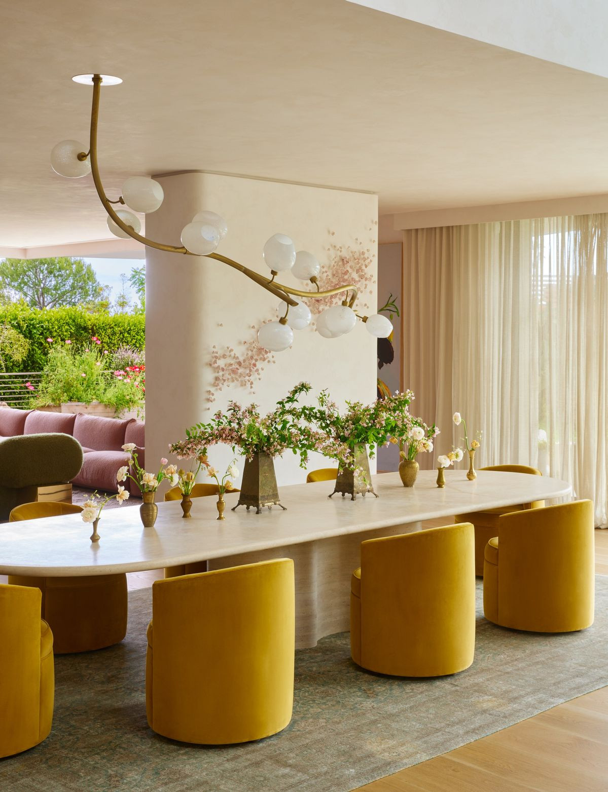 Chrissy Teigen and John Legend’s Jake Arnold t Dining room interior with natural light, neutral color palette, curved chandelier and upholstered mustard chairs in a contemporary Beverly Hills home designed by Jake Arnold.