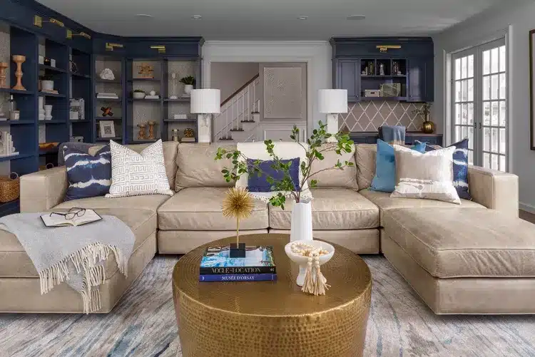 Dark navy floor-to-ceiling built-ins and a large sandy beige leather sectional set the tone for this coastal living room from Curated Nest Interiors.